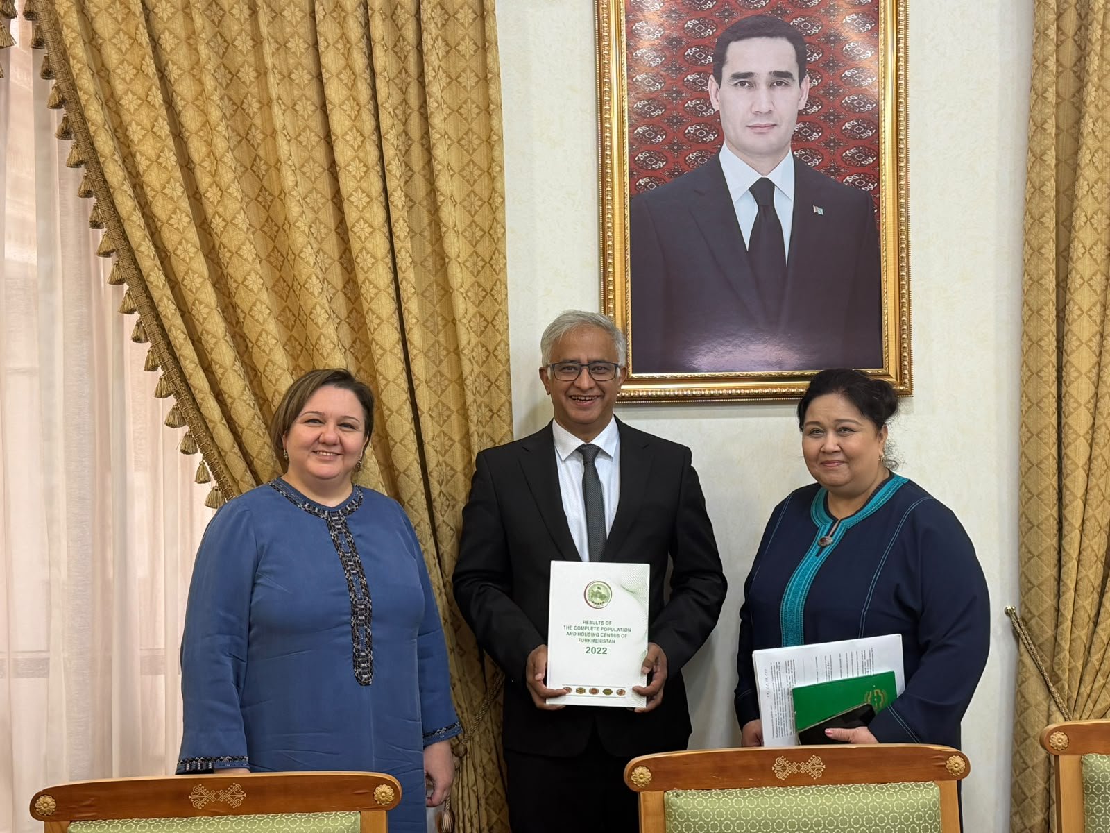 Prof. Samir KC holding the Results of the Complete Population and Housing Census of Turkmenistan 2022, with two colleagues at the State Committee on Statistics