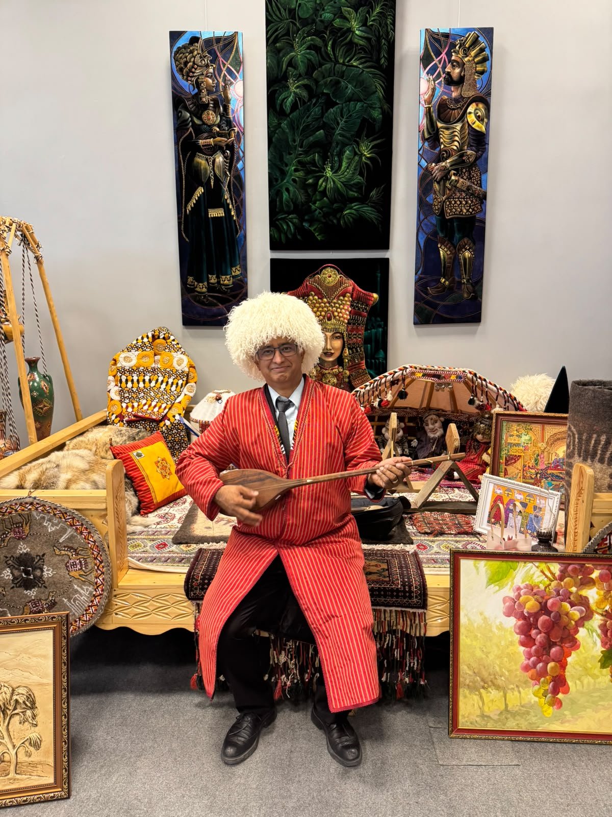 Prof. Samir KC in a Turkmen telpek hat and red robe, holding a dutar